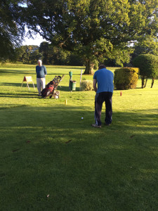 Peter Crosby strikes the first ball in our classic at 8.00am on Friday. watched by team mate Jim Mullery. He is scanning the course for the Third Man.